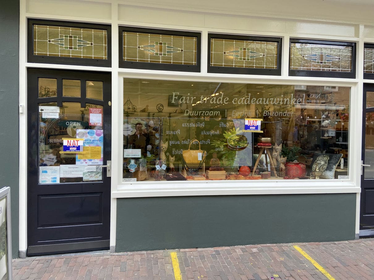Vers geschilderde voorgevel van een fair trade cadeauwinkel in Zoetermeer met klassieke glas-in-loodramen en strak schilderwerk in donkergroen en wit. Het schilderwerk benadrukt de authentieke details van de houten kozijnen en deur.