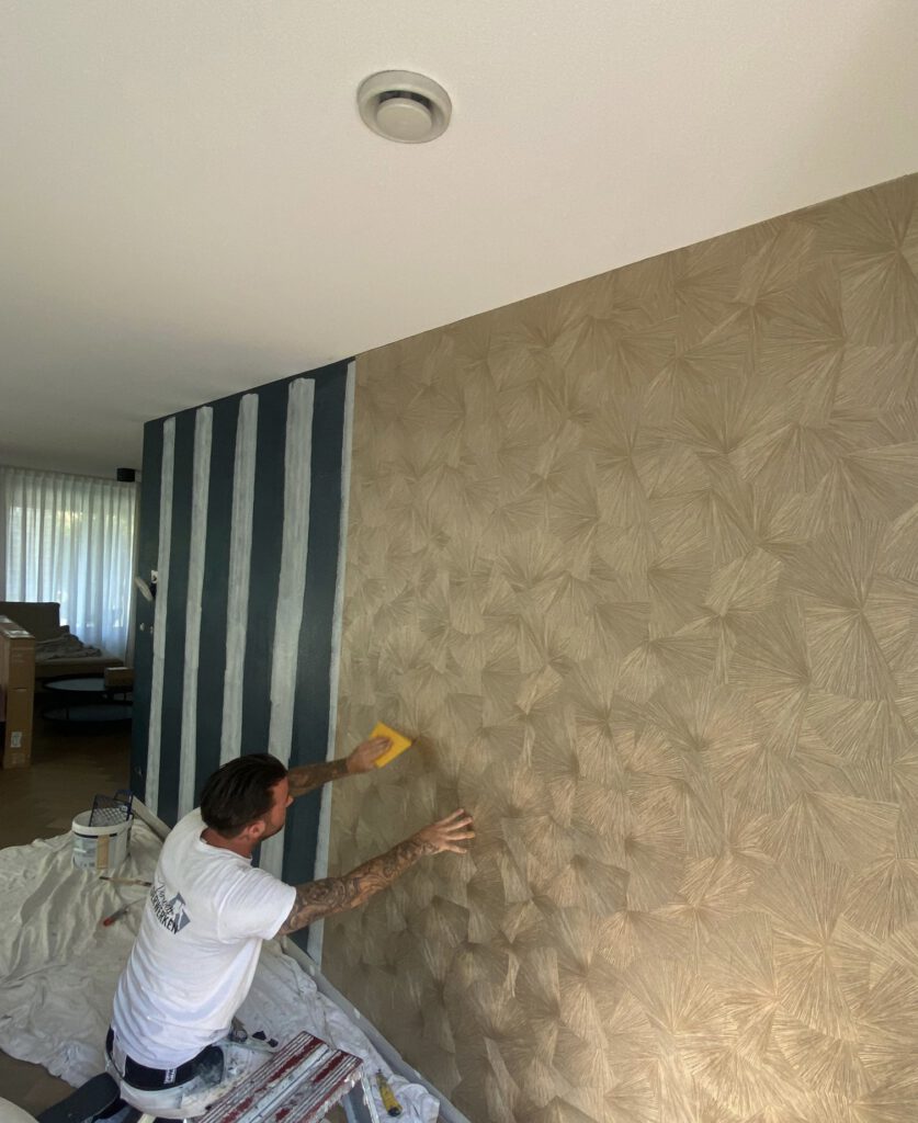 Behanger in Zoetermeer brengt vakkundig exclusief design behang aan met goud- en streeppatroon.