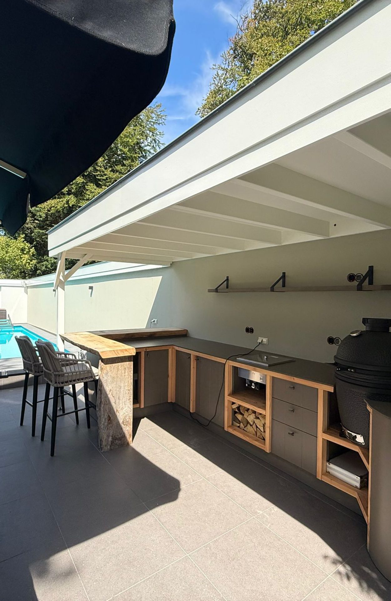 Strak geschilderde buitenkeuken met overkapping en zwembad in moderne tuin.